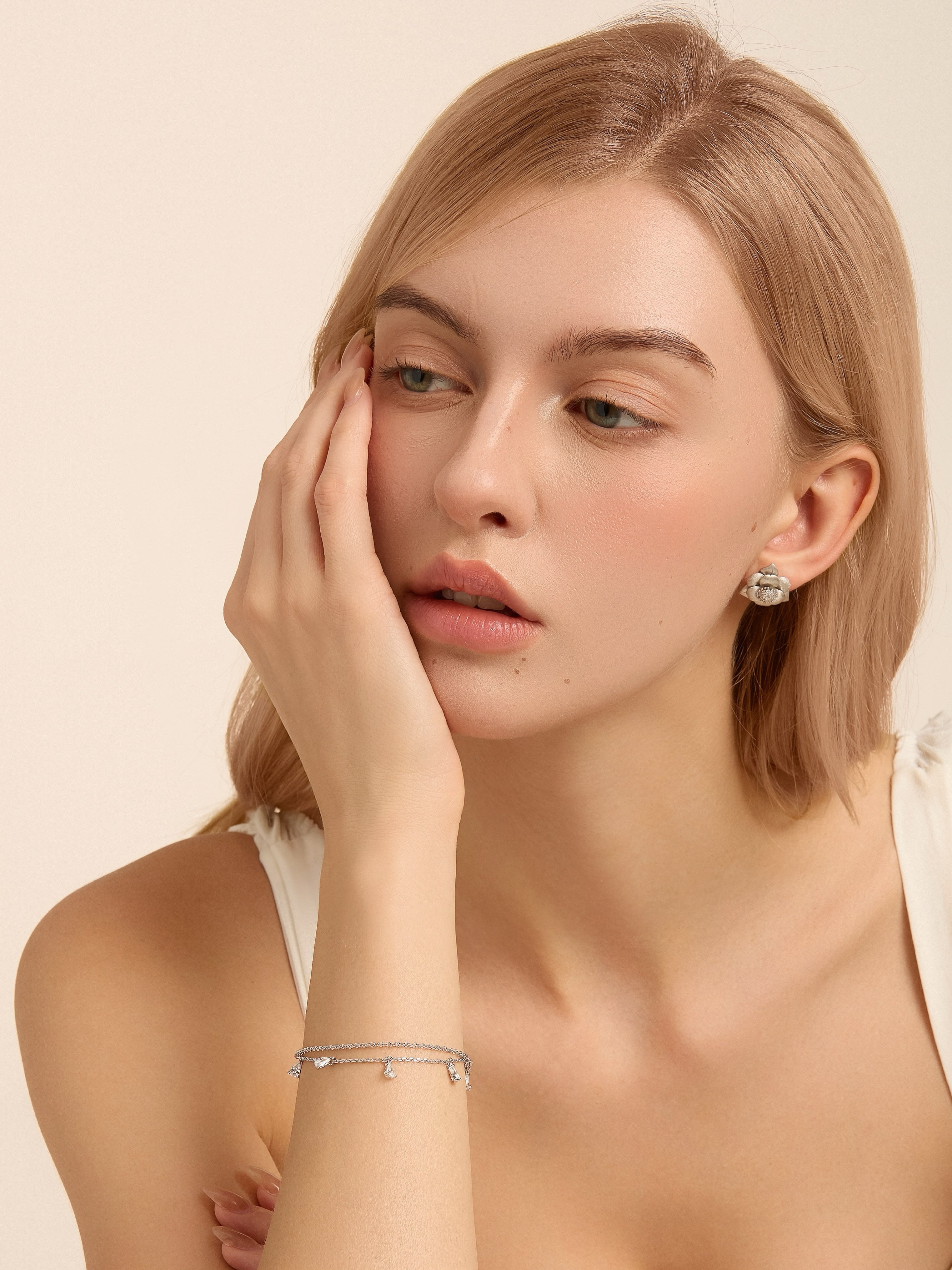 Model in a cream top wearing two silver-tone charm bracelets and a sculptural flower stud earring.
