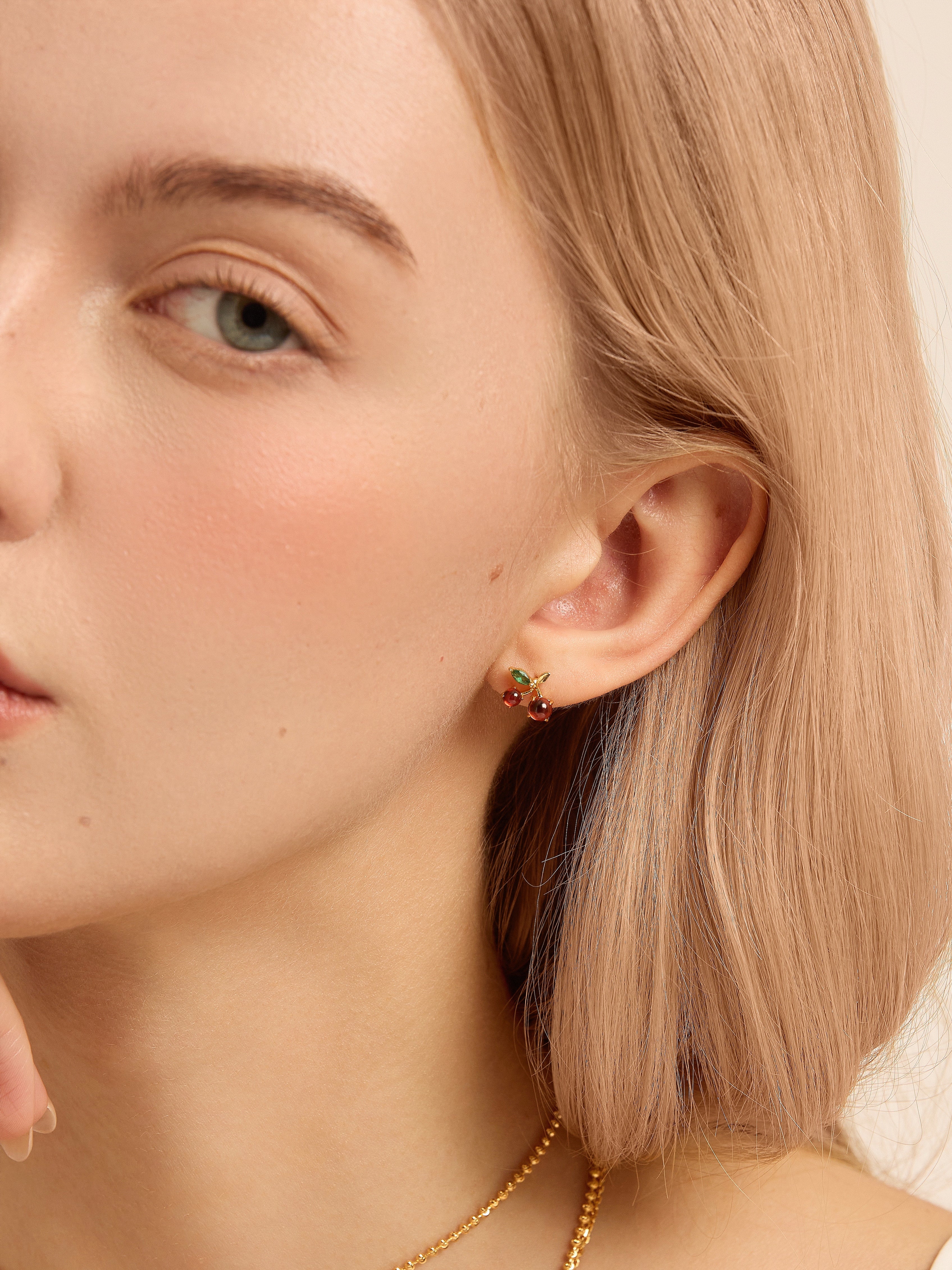 Close-up of a model wearing a gold-tone cherry stud earring with red and green stones.